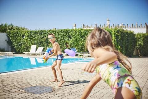 Girl and boy having a water fight with water gun and water bombs at the poolside model released Symbolfoto  DIKF00307
