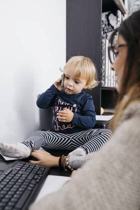 Mother working at home with little daughter sitting on desk holding cell phone model released Symbolfoto property released  JRFF02108