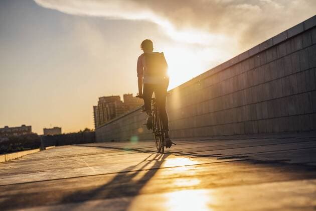 Young man with backpack riding bike on promenade at sunset model released Symbolfoto  VPIF01063