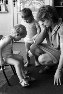 21.08.1985, Berlin, DDR - Erzieherin schaut einem Kleinkind in einer Kinderkrippe beim Anziehen zu. (20-30 Jahre, Alltag, ankleiden, anziehen, auskleiden, ausziehen, Berlin, bis 10 Jahre, DDR, deutsch, Deutsche Demokratische Republik, Deutschland, Erzieherin, Europa, europaeisch, Frau, Ganztagsbetreuung, GDR, Gesellschaft, HF, historisch, Hochformat, innen, Innenaufnahme, Kaukasier, Kaukasierin, kaukasisch, Kinder, Kinderbetreuung, Kindergaertnerin, Kindergarten, Kindergartenalltag, Kindergartenkinder, Kinderkrippe, Kindertagesbetreuung, Kindheit, Kita, Kleinkinder, Menschen, Personen, pmscartandhistory, s w, schwarz weiss, schwarz-weiss, Schwarzweiss, Westeuropa, Wirtschaft, Zeitdokument, Zeitgeschichte, zuschauen, zusehen) 850821KF016KINDERKRIPPE.JPG *** 21 08 1985 Berlin GDR nursery school teacher looks at a toddler in a crèche dressi