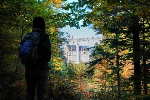 Woman with backpack watching Neuschwanstein castle with Marienbrücke, bridge on October 9, 2018 in Hohenschwangau, Germany. Photographer: Peter Schatz
