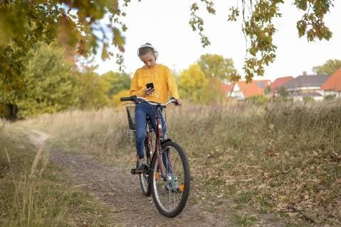 IMAGO Creative, Jahreszeit Herbst, Ferien Girl with headphones sitting on bicycle looking at smartphone model released Symbolfoto  BFRF01951