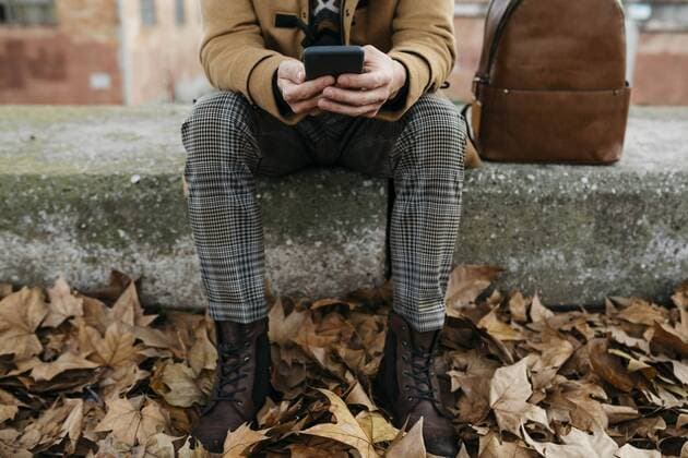 Spain, Igualada, close-up of man sitting down using cell phone surrounded by autumn leaves model released Symbolfoto  JRFF02300