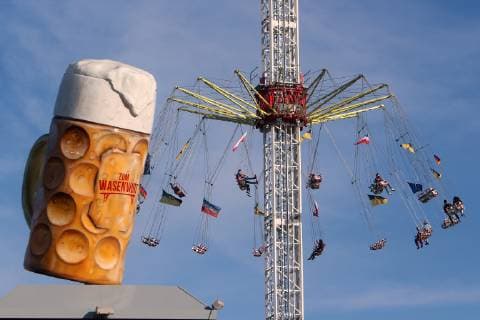 Cannstatter Wasen Spring festival on Easter Sunday in Stuttgart Bad Cannstatt Baden Württemberg Germany oversized glass of beer Wasenwirt on the roof of a marquee it in front of a spinning ride s under a bright blue sky