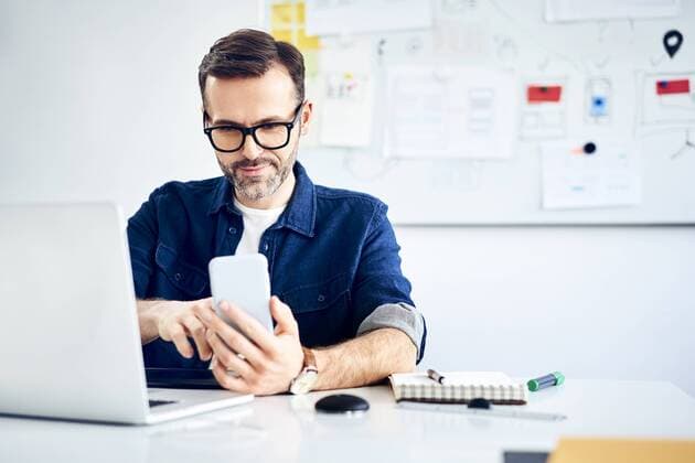 Casual businessman using smartphone and laptop at desk in office model released Symbolfoto  BSZF01014
