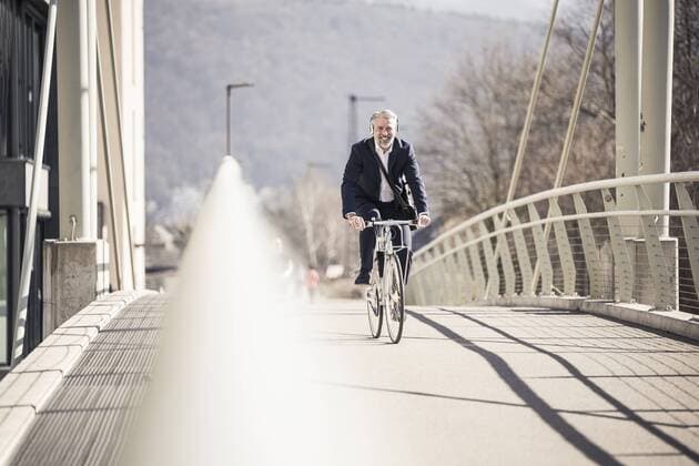 Smiling mature businessman with headphones riding bicycle on a bridge in the city model released Symbolfoto  UUF16637