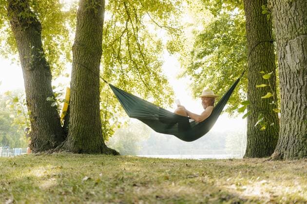 Senior man wearing straw hat relaxing in hammock at lakeshore reading book model released Symbolfoto property released  GUSF01786