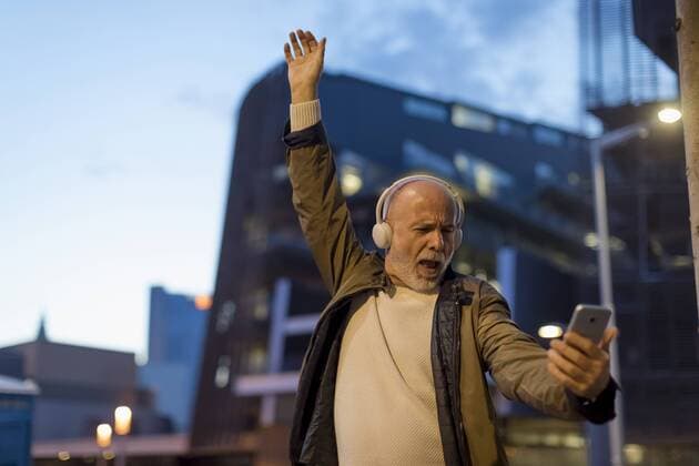 Spain, Barcelona, excited senior man with headphones and cell phone in the city at dusk model released Symbolfoto  MAUF02272