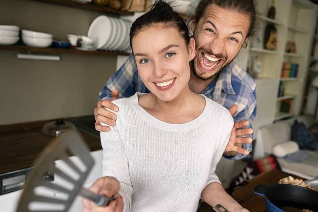 Young couple preparing food together, laughing and pointing with spatula model released Symbolfoto property released  PESF01229