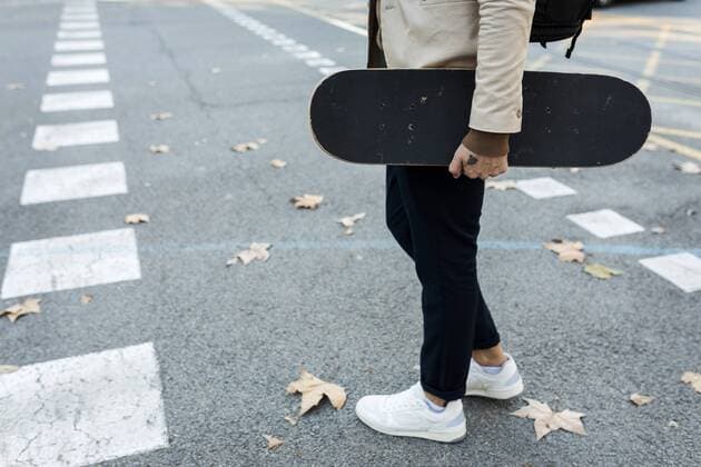 Man with backpack and skateboard crossing the street in autumn, partial view model released Symbolfoto  VABF02091