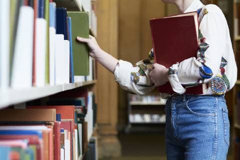 Female student with a book in a public library, choosing one model released Symbolfoto  IGGF01031