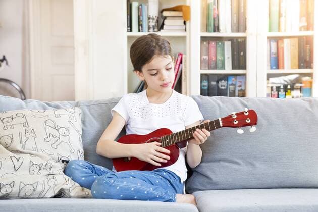 Portrait of girl sitting on couch at home playing ukulele model released Symbolfoto property released  LVF07926