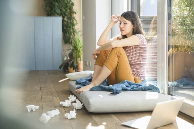 Sad young woman sitting at the window at home with laptop and tissues model released Symbolfoto property released  UUF17008