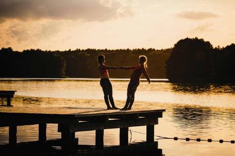 Women practicing acro yoga on tranquil sunset lake dock Germany Mecklenburg-Vorpommern Barnin  Copyright: SvenxHagolani fStopImages1818036