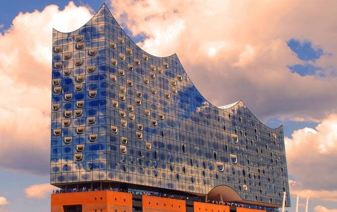 Clouds and a blue sky are reflected in the façade of the Elbe Philharmonic Hall in Hamburgs harbour Bearbeitet