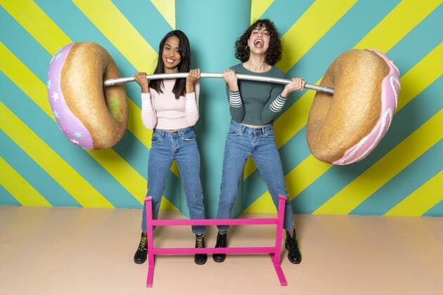 Two happy young women at an indoor theme park having fun with oversized donuts model released Symbolfoto property released  AFVF02815