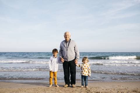 Portrait of happy grandfather standing hand in hand on the beach with his grandchildren model released Symbolfoto  JRFF03231