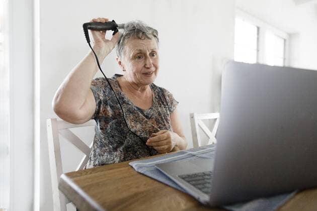Senior woman sitting at table at home using laptop and doing her hair model released Symbolfoto property released  KMKF00924