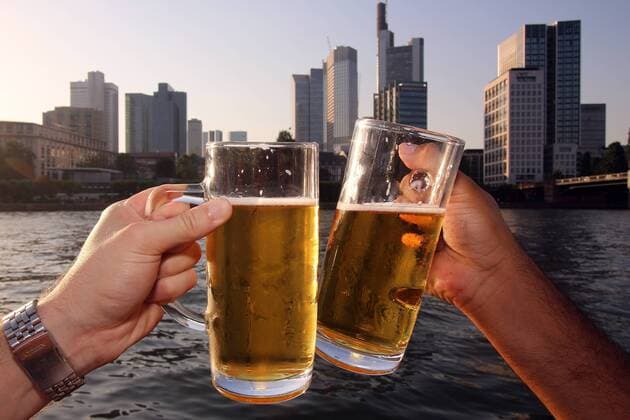 Two men enjoy a warm summer evening on the banks of the Main in front of the banking district and toast with a beer, Frankfurt, Hesse, Germany