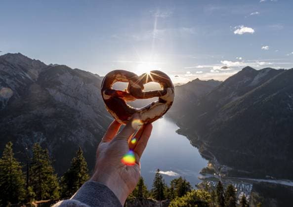  Food, Brezel Hand hält bayrische Breze vor Alpenpanorama, Blick vom Schönjöchl auf Plansee, Tirol, Österreich, Europa *** Hand holding Bavarian Breze in front of Alpine panorama, view from Schönjöchl to Plansee, Tyrol, Austria, Europe Copyright: imageBROKER/MoritzxWolf ibxmmw04917568.jpg