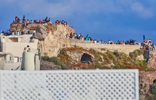 Tourists on Oia Castle wait for the sunset with Caldera View and the famous Windmill in Oia, Santorini , Greece at 04 June 2019. Photographer: Peter Schatz