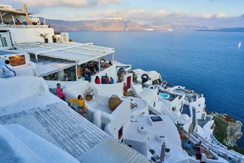 Tourists in restaurants and on Oia Castle wait for the sunset with Caldera View and the famous Windmill in Oia, Santorini , Greece at 04 June 2019. Photographer: Peter Schatz