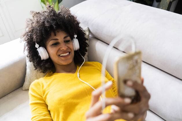 Smiling woman lying on couch with cell phone and headphones model released Symbolfoto property released  GIOF06488