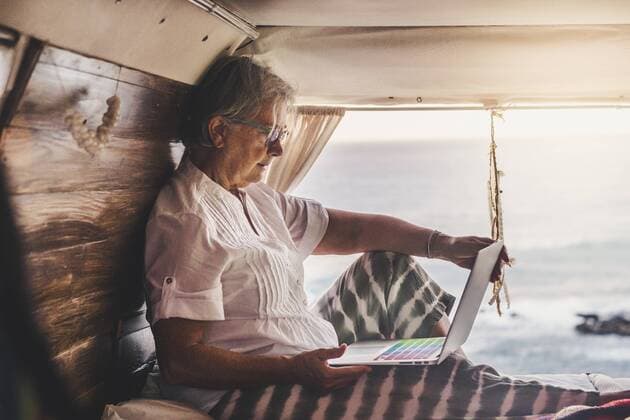Senior woman sitting in vintage van by he sea, using laptop model released Symbolfoto  SIPF02012