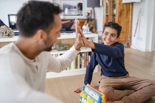 Father and son sitting on the floor at home playing a game and high fiving model released Symbolfoto property released  DIGF07769