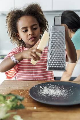 Girl cooking with mother in kitchen grating cheese model released Symbolfoto property released  ERRF01683