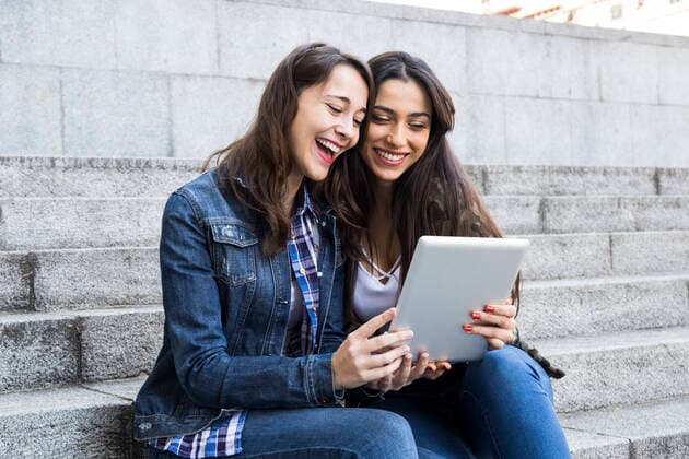 Happy young women watching tablet sitting on steps together in Madrid, Spain model released Symbolfoto  ABZF02486