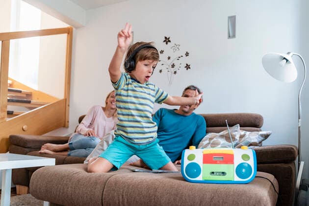 Excited boy listening to music with headphones on couch at home with parents in background model released Symbolfoto property released  DIGF08202