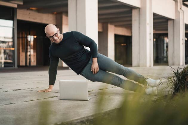 Portrait of smiling man doing pushups while looking at laptop model released Symbolfoto  KNSF06207
