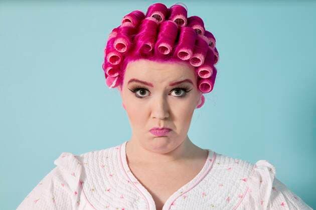 Portrait of young woman grimacing with hair curlers over colored background,model released, Symbolfoto 03C05276