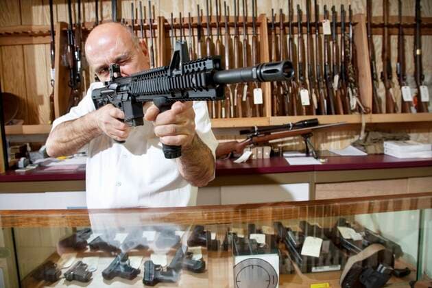 Mature merchant aiming with rifle in gun shop,model released, Symbolfoto,property released 03C05480