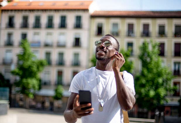 Smiling young man using smartphone and ear phones, looking up model released Symbolfoto  CJMF00141