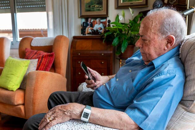Elderly man using a mobile phone and wearing a smart emergency alarm bracelet around wrist at home model released Symbolfoto property released  GEMF03152