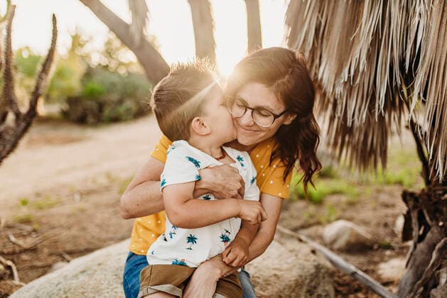 Young son embracing and kissing mom on rock in sunny cactus garden United States, California, San Diego CR_KESM191001B-162306-01