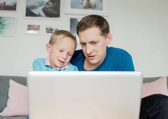 father and soon smiling looking at a laptop at home together Sweden, Stockholm County, Norrtälje CR_RABE191022-210173-01