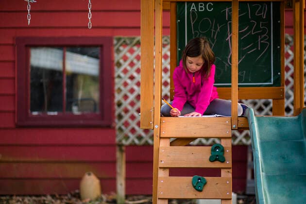 A little girl sits in a playset writing in a notebook with a pencil United States, Ohio, Columbus CR_RETI190924-153257-01