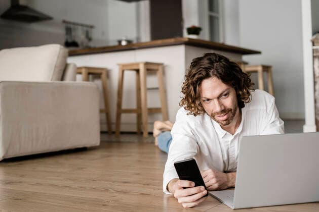 Man lying on the floor at home using cell phone and laptop model released Symbolfoto property released  GIOF07516