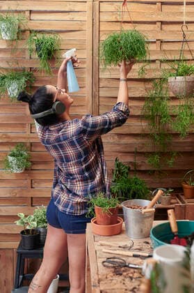 Happy woman spraying water on plants on her terrace while listening to music model released Symbolfoto property released  IGGF01393
