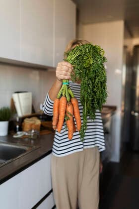 Woman holding a bunch of carrots in kitchen at home model released Symbolfoto property released  VABF02438