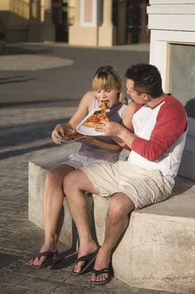 Young couple eats a pizza slice Young couple eating pizza outdoors
