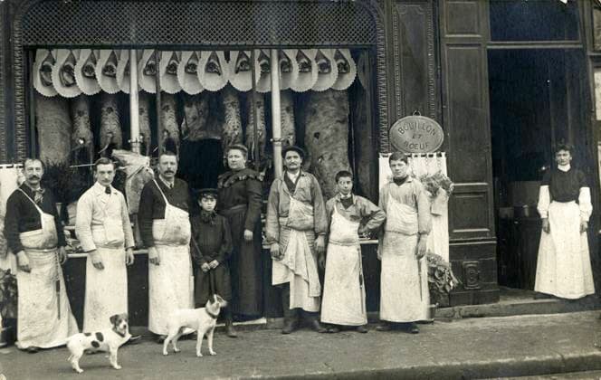 BOUCHERIE annees 1900 Groupe de personnes, dont des bouchers en tabliers devant une boucherie et des carcasses d animaux suspendues. Photographie anonyme pour une carte postale vers 1905. Credit : Collection IM KHARBINE-TAPABOR *** 1900s Butchery Group of people, including butchers in aprons in front of a butcher shop and hanging animal carcasses Anonymous photograph for a postcard around 1905 Credit Collection IM KHARBINE TAPABOR  KH177411