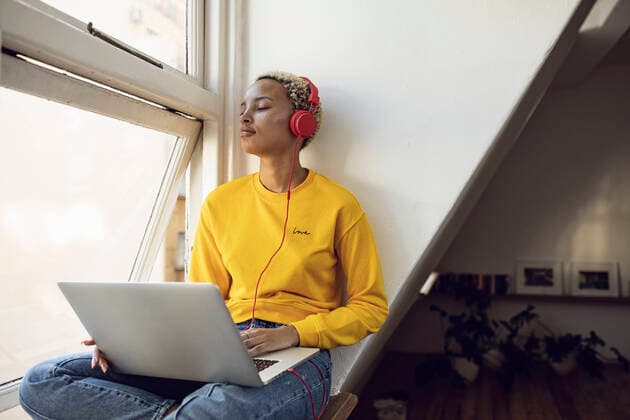 Young woman sitting at the window at home with laptop and headphones model released Symbolfoto property released  MCF00407