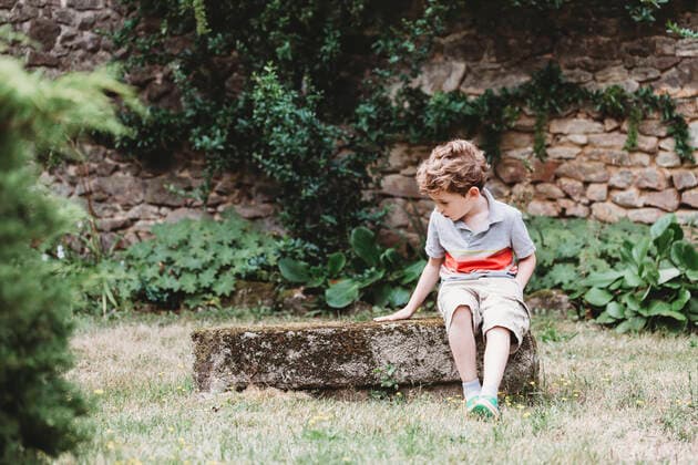 Front view of boy sitting on moss-covered rock-bench Champagnat, Dompierre-Les-Eglises, France CR_CEHE191104A-198722-01