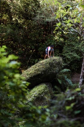 Preteen boy climbing on green rocks in forest Hawke s Bay, New Zealand CR_JUCR191116-239764-01
