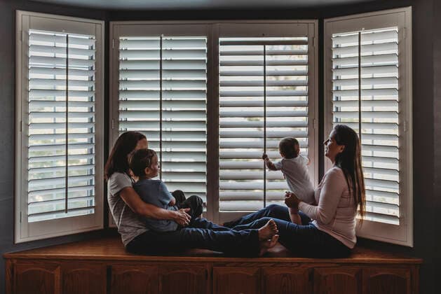 Same sex parents lounging with kids on window seat with tall shutters La Mesa, CA CR_KESM191114A-213342-01