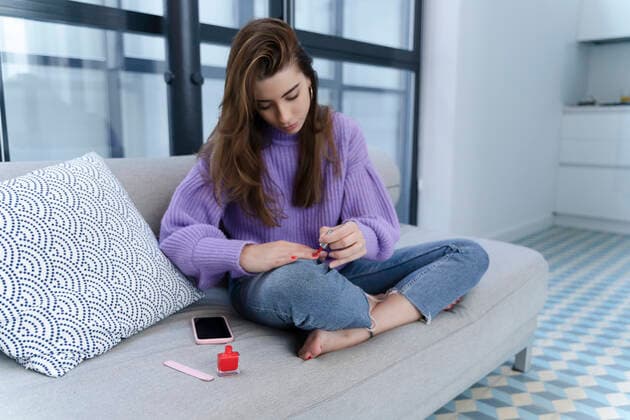 IMAGO Creative: Jahreszeit Winter, Couching Young woman sitting on couch applying nail varnish model released Symbolfoto property released  ERRF02589